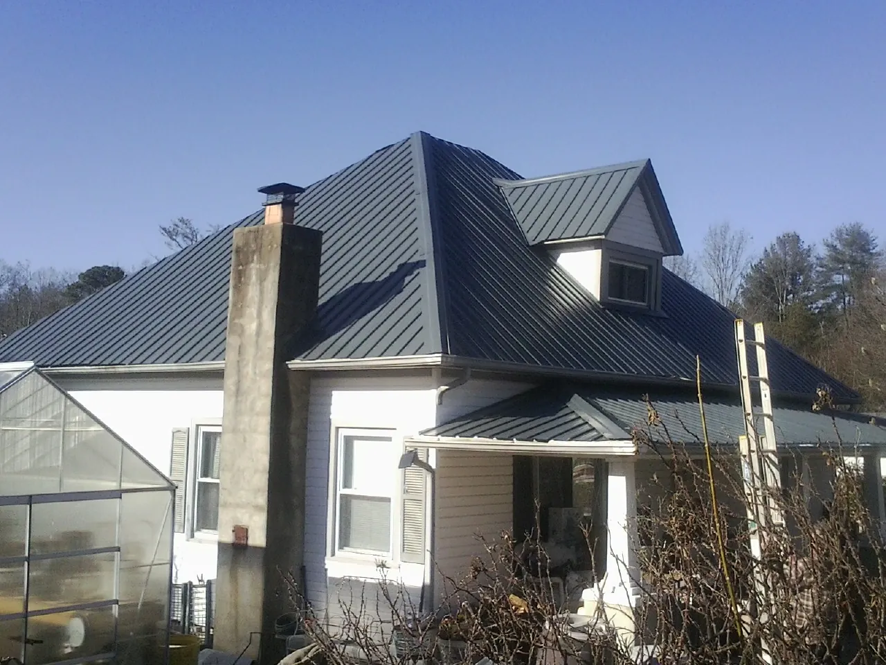 Dark blue standing seam metal roof on a white farmhouse with dormer — Slate & Tile Roof Repair by Roofing Brothers in Lowell