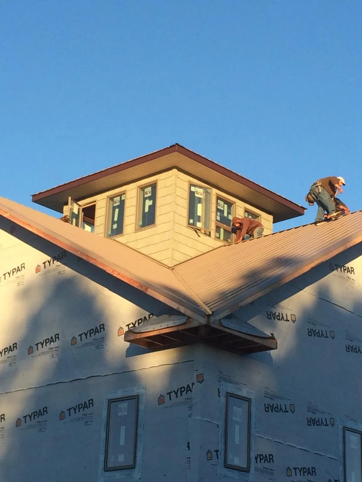 Roofers working around a rooftop cupola on a new metal roof at sunset — Roof Waterproofing in Lowell by Roofing Brothers